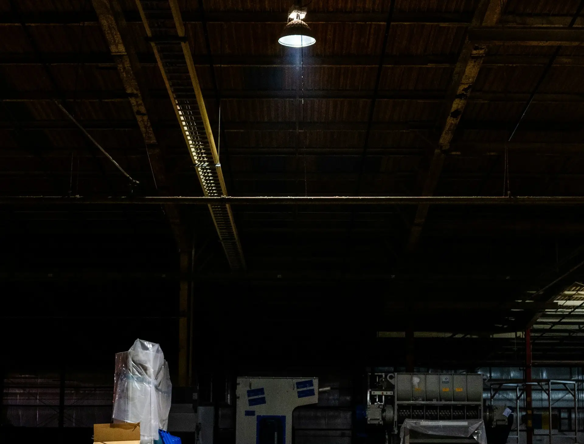 Insights Blog 2 Dimly lit industrial warehouse interior with overhead light and machinery.