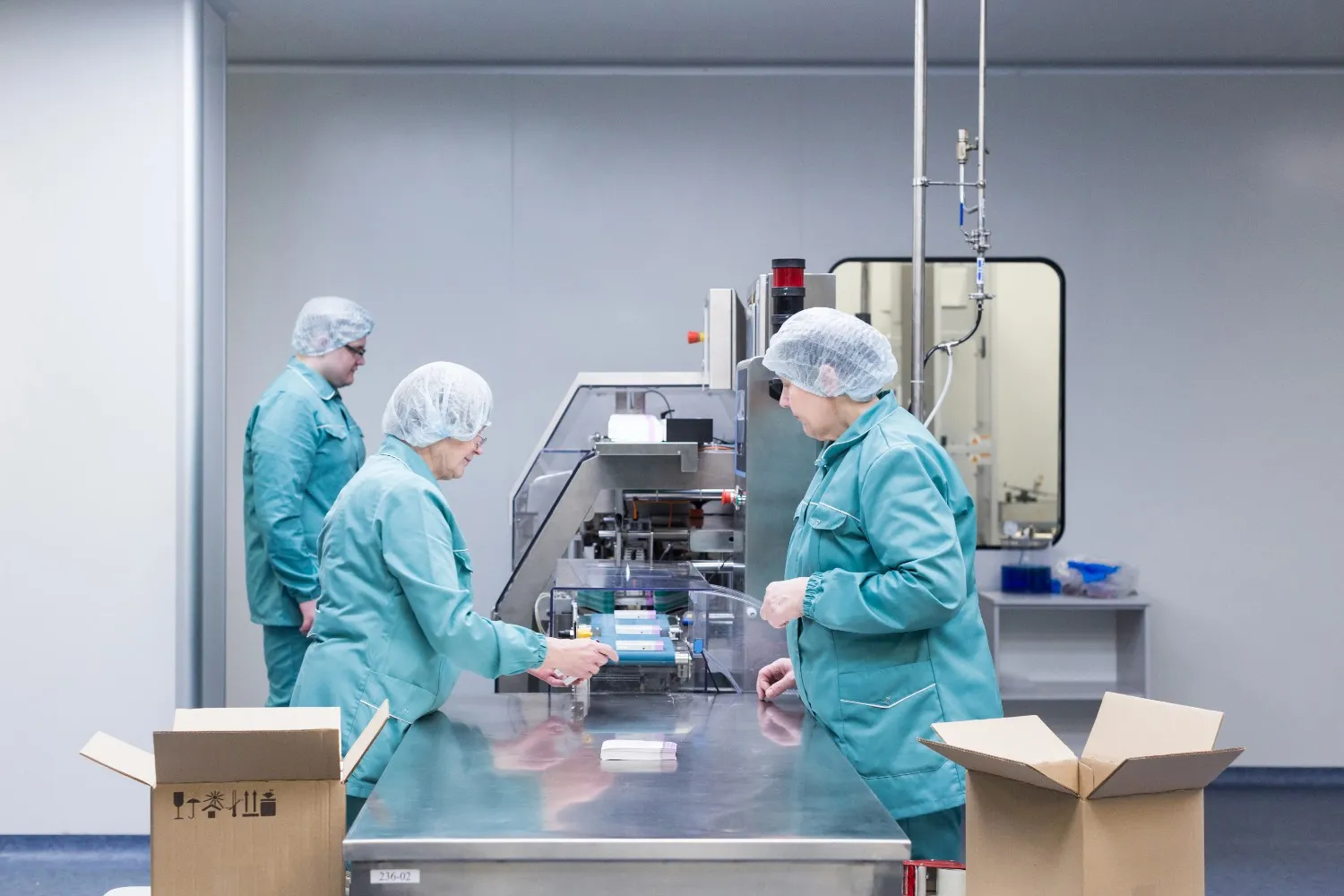 Insights Blog 4 Pharmaceutical workers in protective clothing operating packaging equipment in a cleanroom, highlighting controlled manufacturing and environmental risk management.