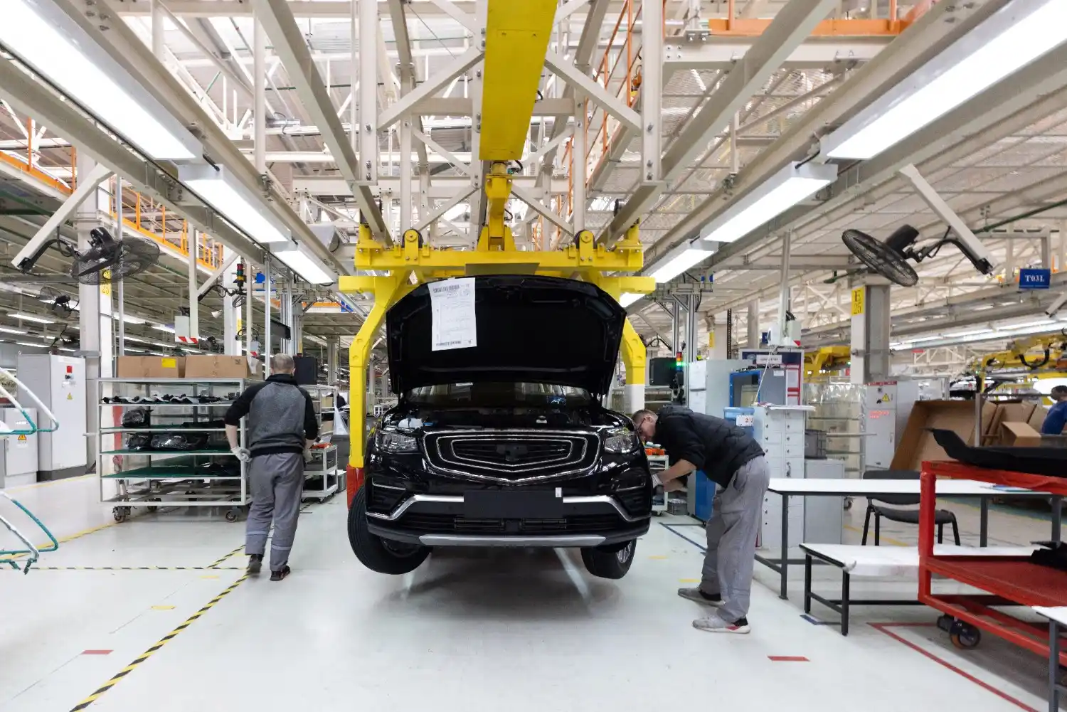 Insights Blog 7 Automotive assembly line with workers inspecting a car under a lifting frame inside a vehicle manufacturing plant.