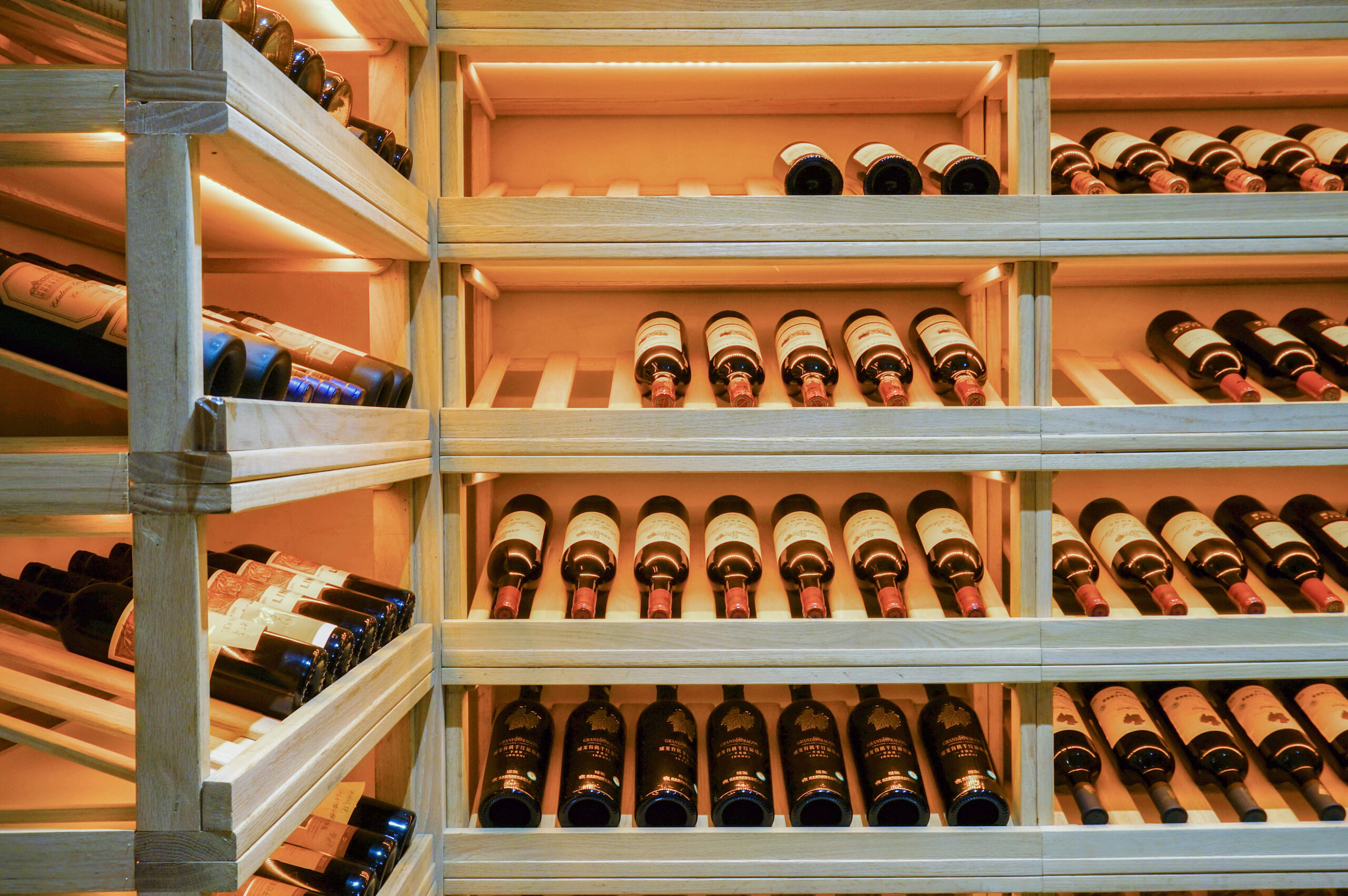Insights Blog 5 Wine cellar with rows of red wine bottles stored horizontally on illuminated wooden racks, showcasing proper humidity conditions for aging.