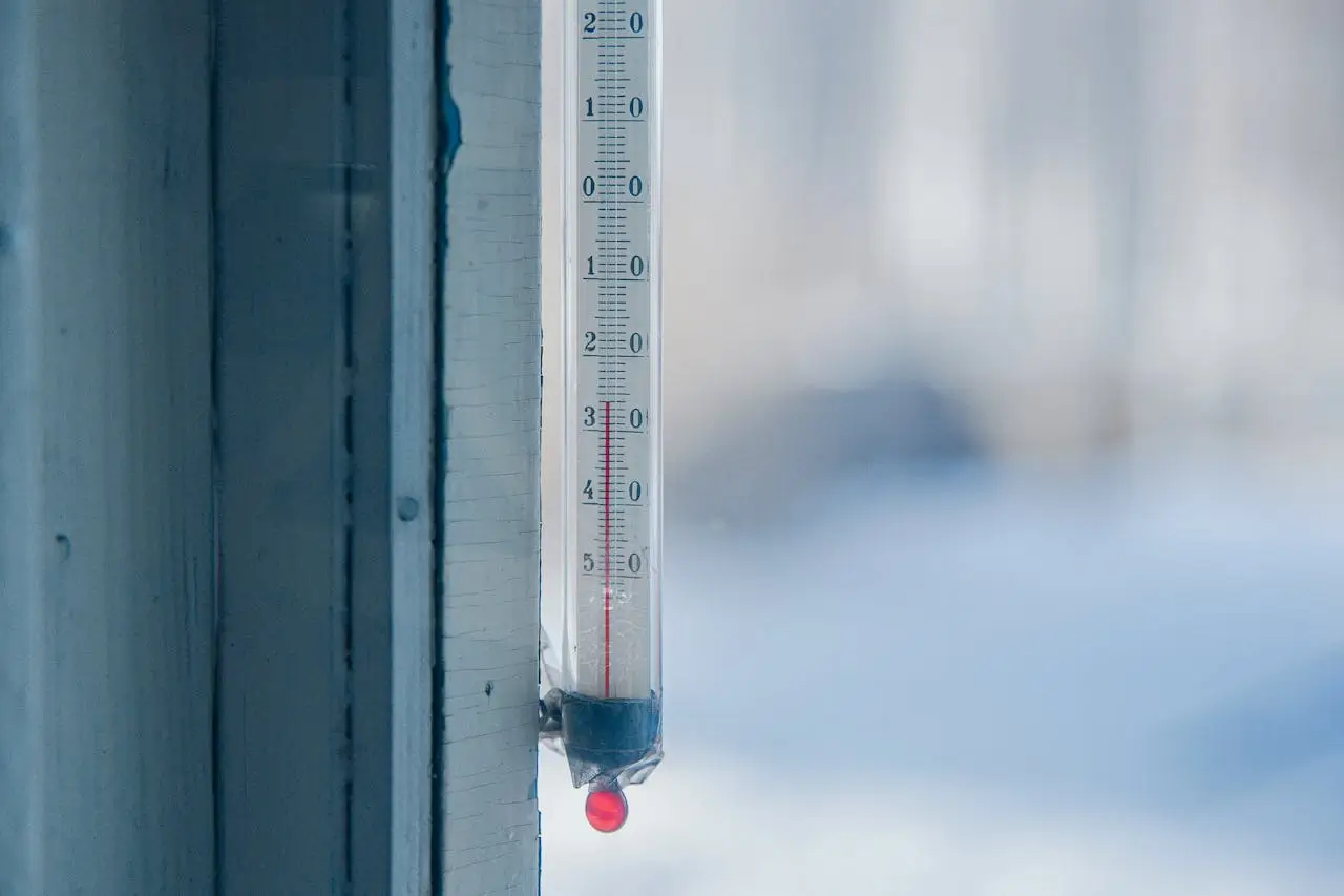 An outdoor thermometer mounted on a wall in cold, humid conditions, illustrating the relationship between measured air temperature and relative humidity.