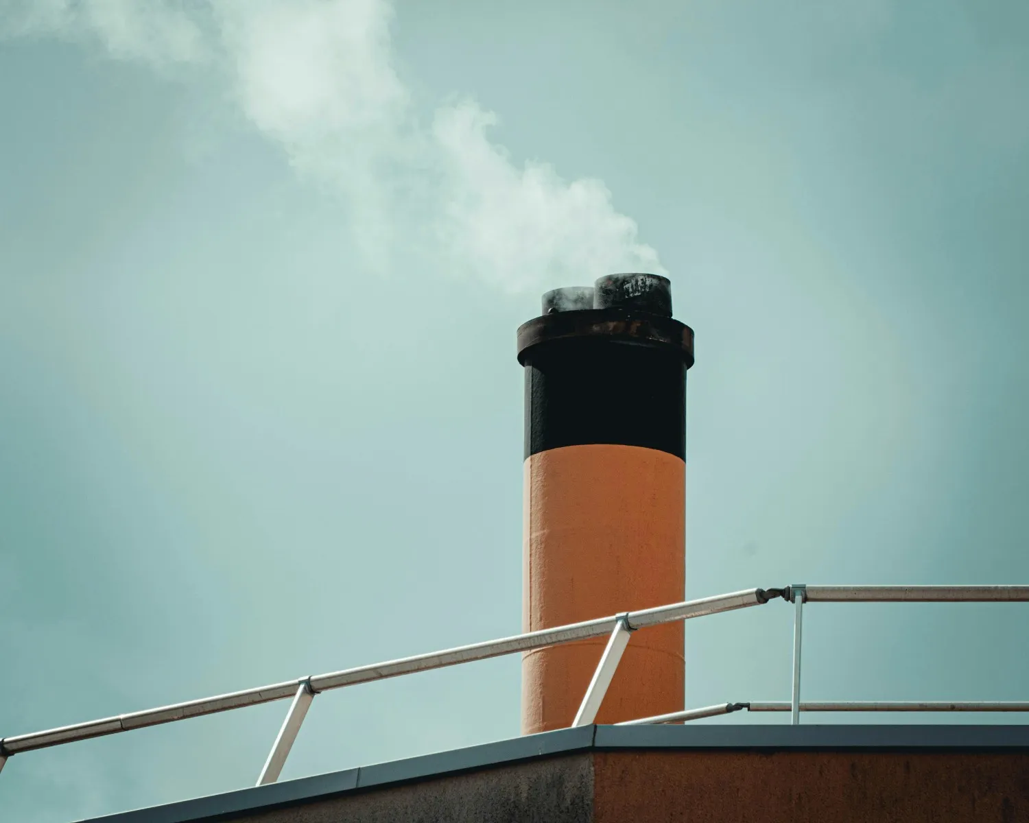 Insights Blog 3 Industrial chimney emitting white steam or smoke against an overcast sky, illustrating airborne emissions that fog-based dust suppression systems are designed to control in industrial facilities.