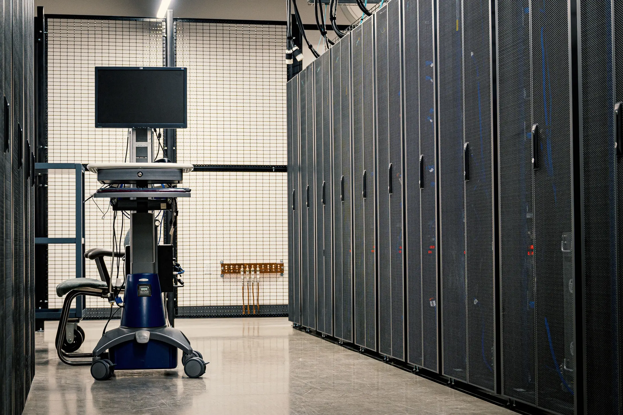 Aisle of server racks inside a modern data center with cooling infrastructure, network equipment, and a mobile workstation positioned between high-density computing cabinets.