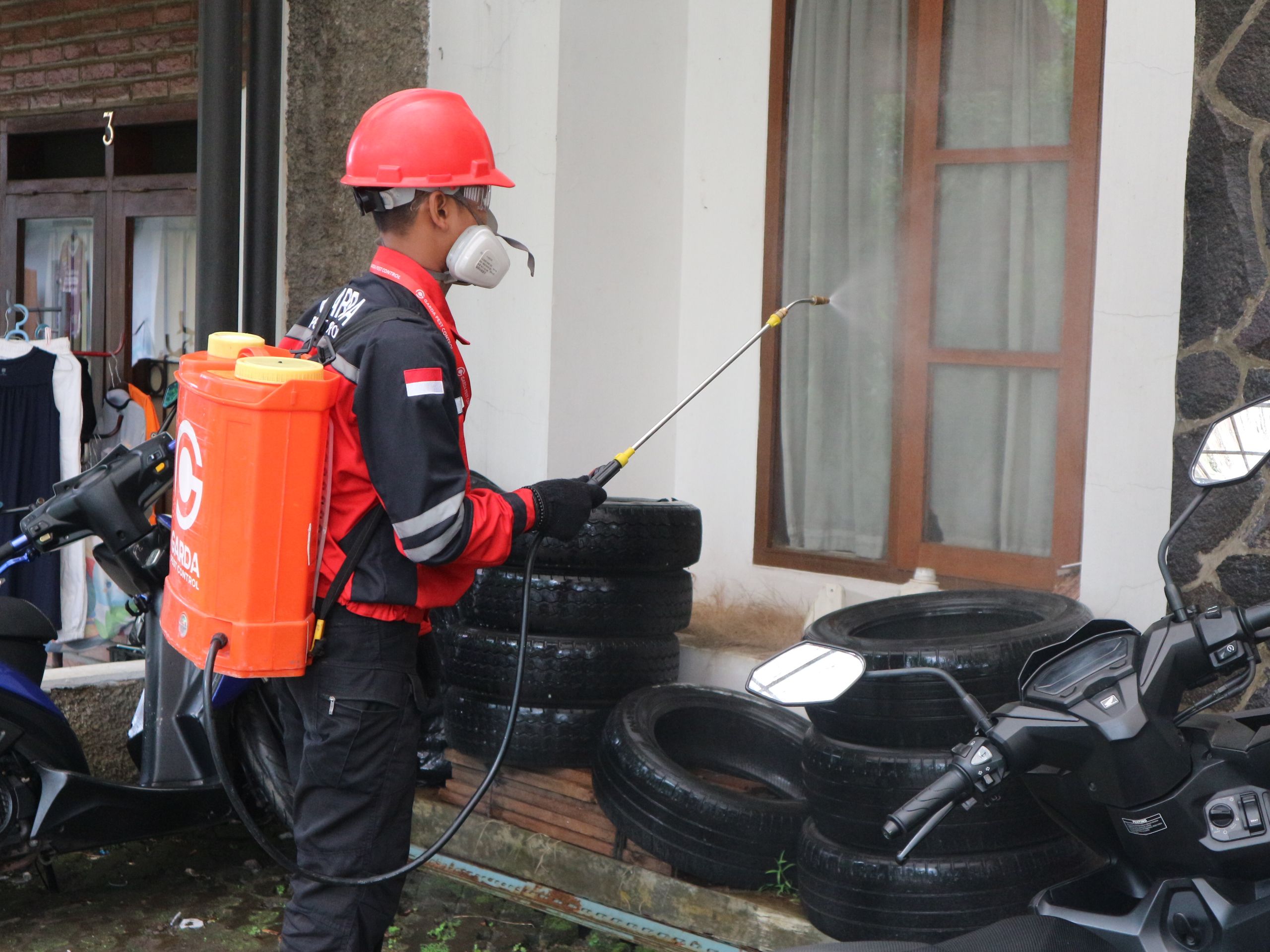 Insights Blog 5 Pest control technician wearing protective equipment and a respirator uses a backpack sprayer to apply disinfectant or pest control treatment around a residential property.