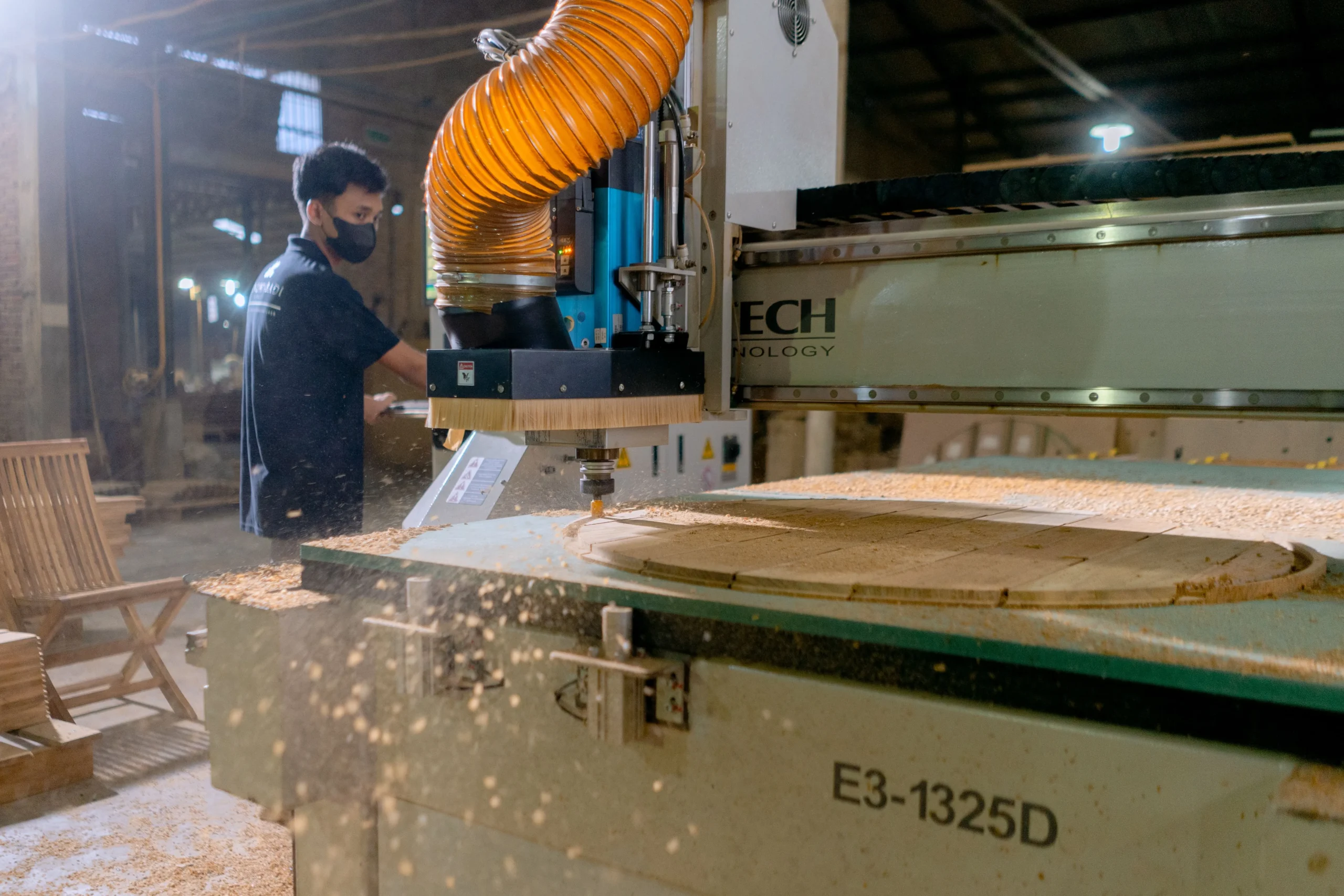 Insights Blog 3 CNC woodworking machine cutting a timber panel in a manufacturing facility, generating sawdust and fine wood particles that require effective dust suppression, static control, and air quality management.