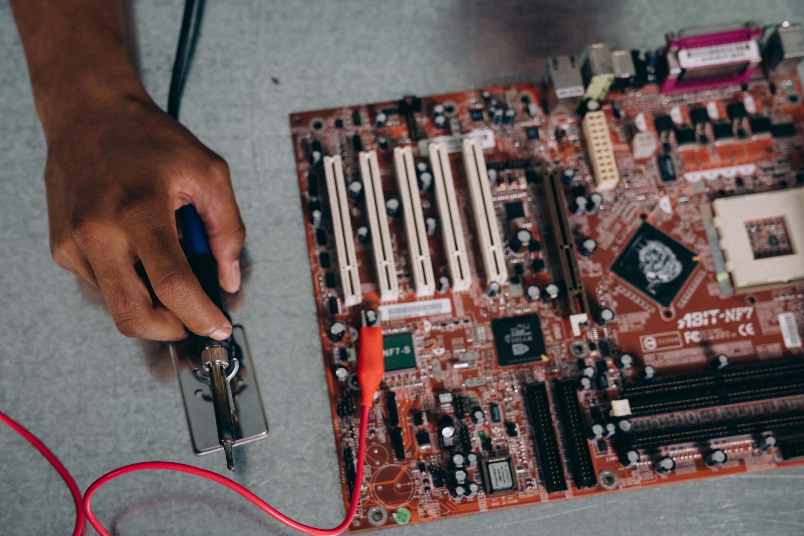 Insights Blog 5 Technician holding a soldering iron beside a printed circuit board during electronics assembly and testing.