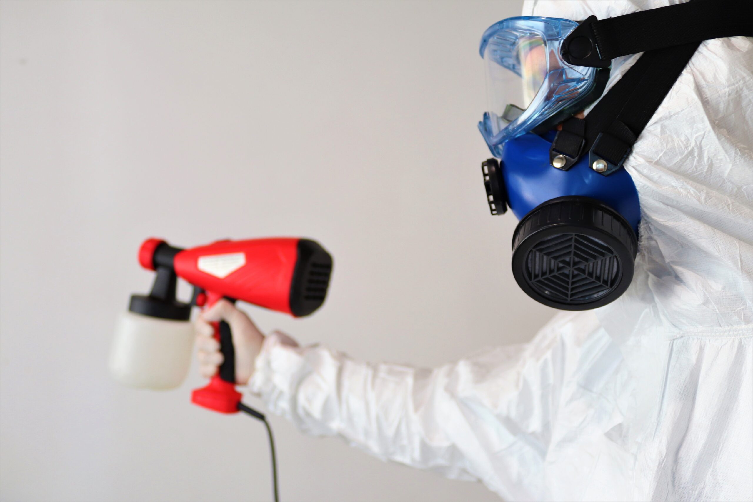 Insights Blog 7 Worker wearing protective coveralls, goggles, and a respirator using an electrostatic sprayer to apply disinfectant in an indoor environment.