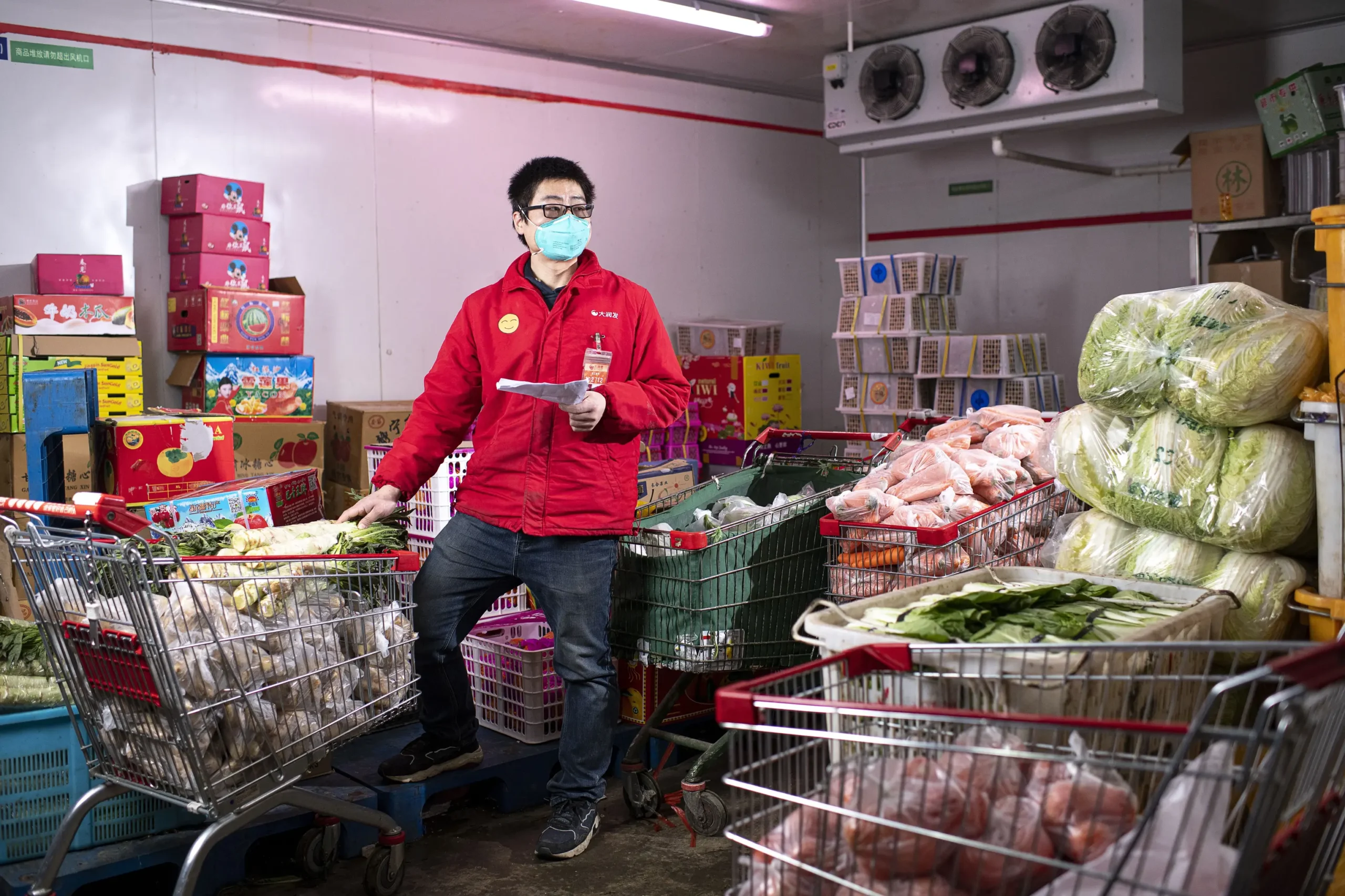 Insights Blog 6 Worker inspecting fresh vegetables inside a refrigerated produce storage room with carts of leafy greens, carrots, and packaged produce, illustrating commercial cold storage operations.