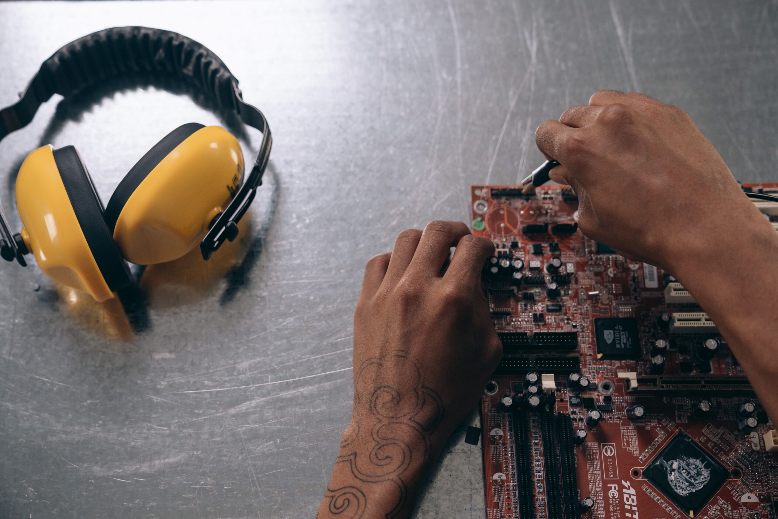 Insights Blog 7 Technician inspecting a printed circuit board on an electronics workbench with hearing protection nearby.