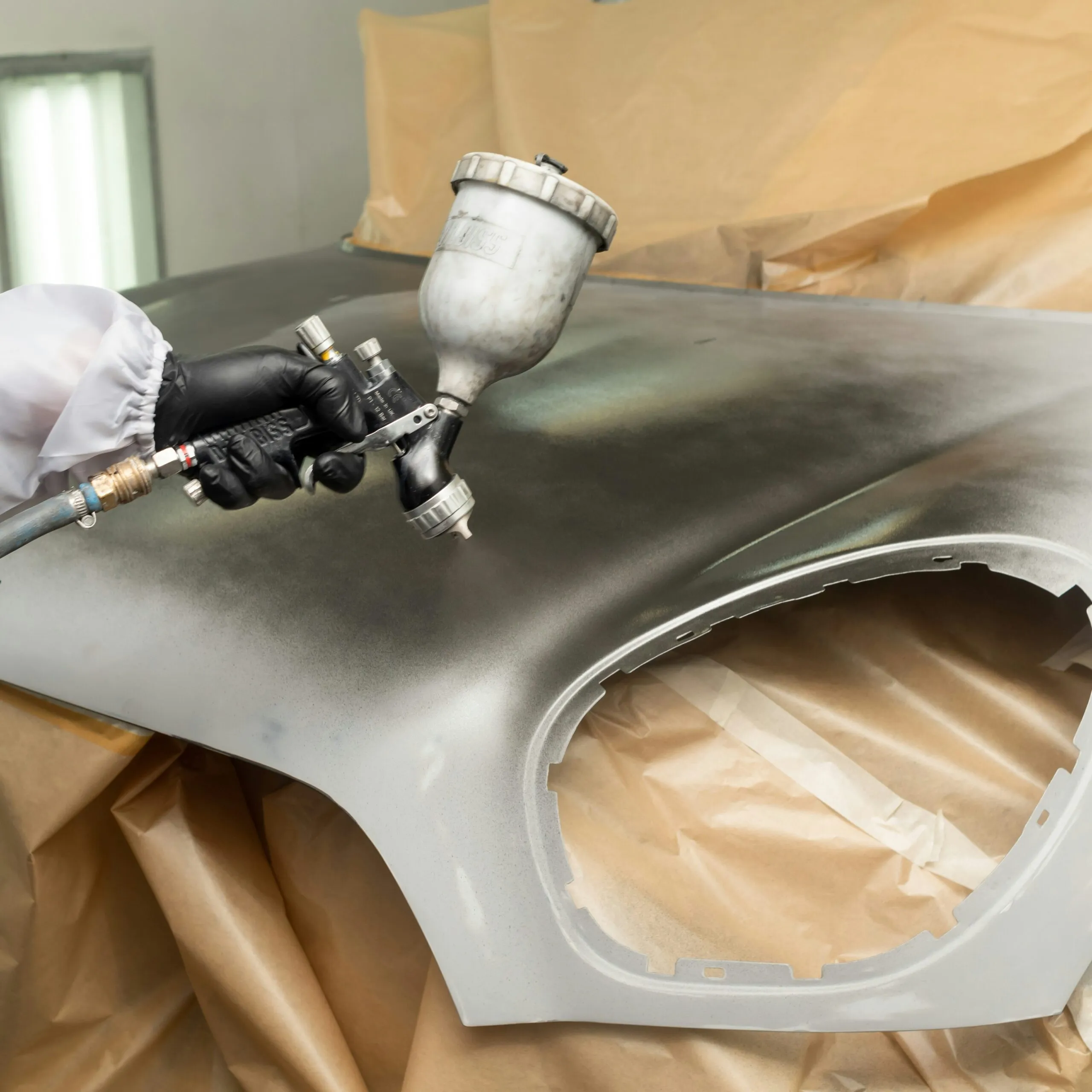 Spray painting a metal panel, representing the coating application affected by dew point and surface temperature compliance.