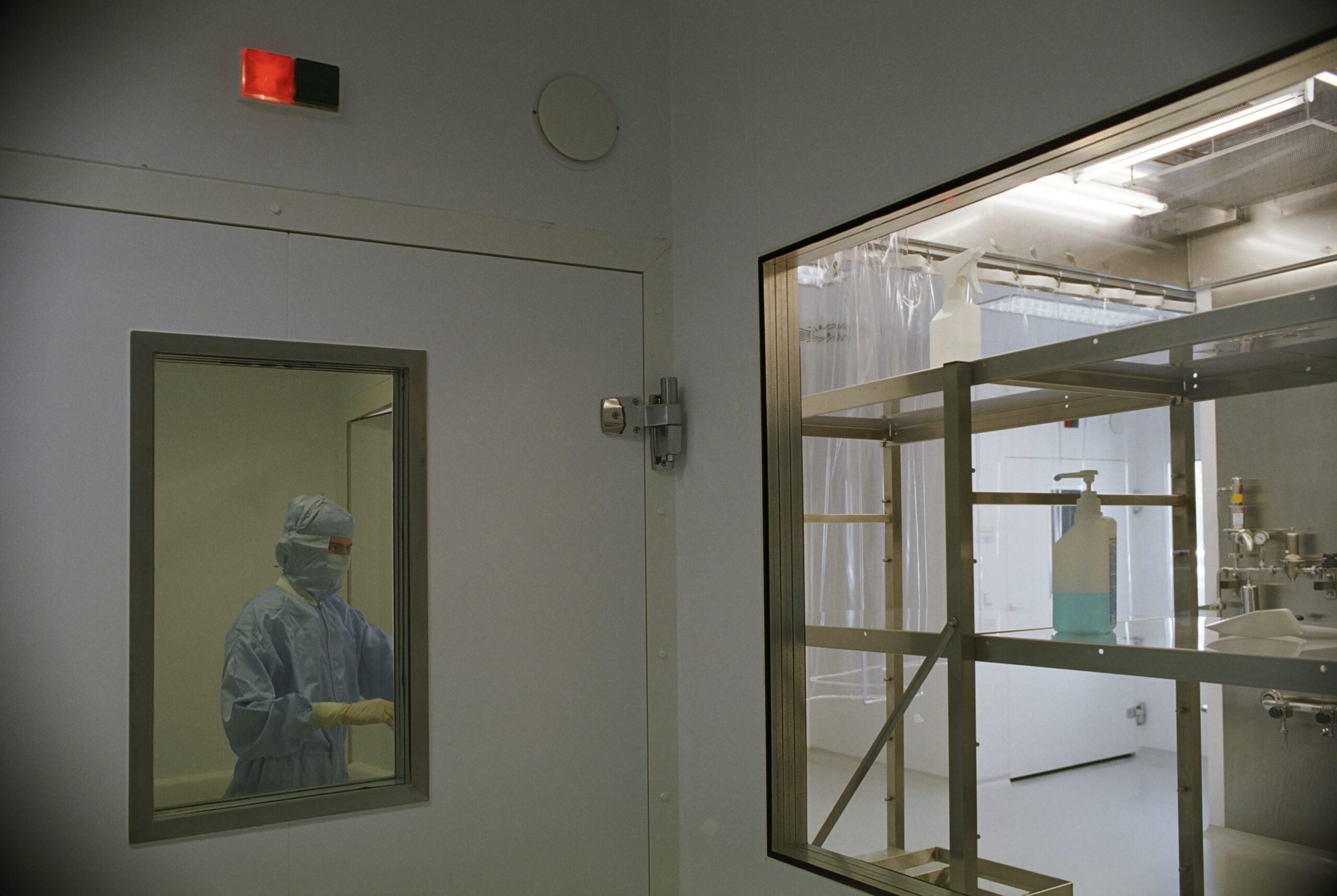 Insights Blog 6 Cleanroom technician viewed through a window, illustrating the controlled environment cleanroom HVAC systems must maintain continuously